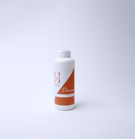 A white plastic bottle with an orange label on a plain white background. The label features text including the word 'Cleanser' and a logo with minimalistic design. The bottle has a screw cap and is positioned slightly to the left of the center.