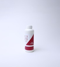 A white plastic bottle with a red and white label featuring text. The bottle has a screw cap and is standing on a white surface with a light background, suggesting a clean and minimal presentation.