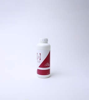 A white plastic bottle with a red and white label featuring text. The bottle has a screw cap and is standing on a white surface with a light background, suggesting a clean and minimal presentation.