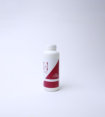 A white plastic bottle with a red and white label featuring text. The bottle has a screw cap and is standing on a white surface with a light background, suggesting a clean and minimal presentation.