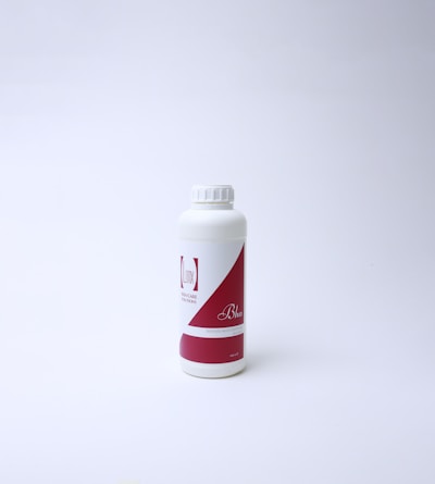 A white plastic bottle with a red and white label featuring text. The bottle has a screw cap and is standing on a white surface with a light background, suggesting a clean and minimal presentation.