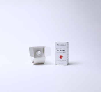 A skincare product displayed against a plain white background. On the right, a box labeled 'Anti-Dark Spot Serum' with a droplet graphic is standing upright. To the left of the box, the box is open and reveals a white bottle nestled inside.