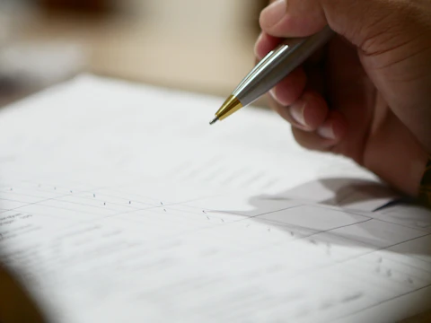 Person working on a laptop surrounded by scattered documents and data sheets