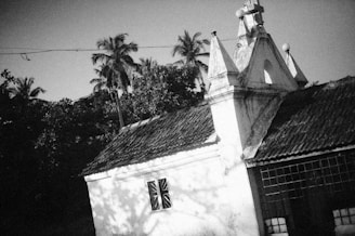 A vintage black and white photo of Rotawa Muslim Maha Vidyalaya's very first building surrounded by lush greenery.