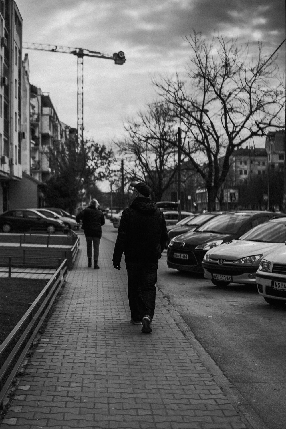 Un par de personas caminando por una acera al lado de una calle con coches