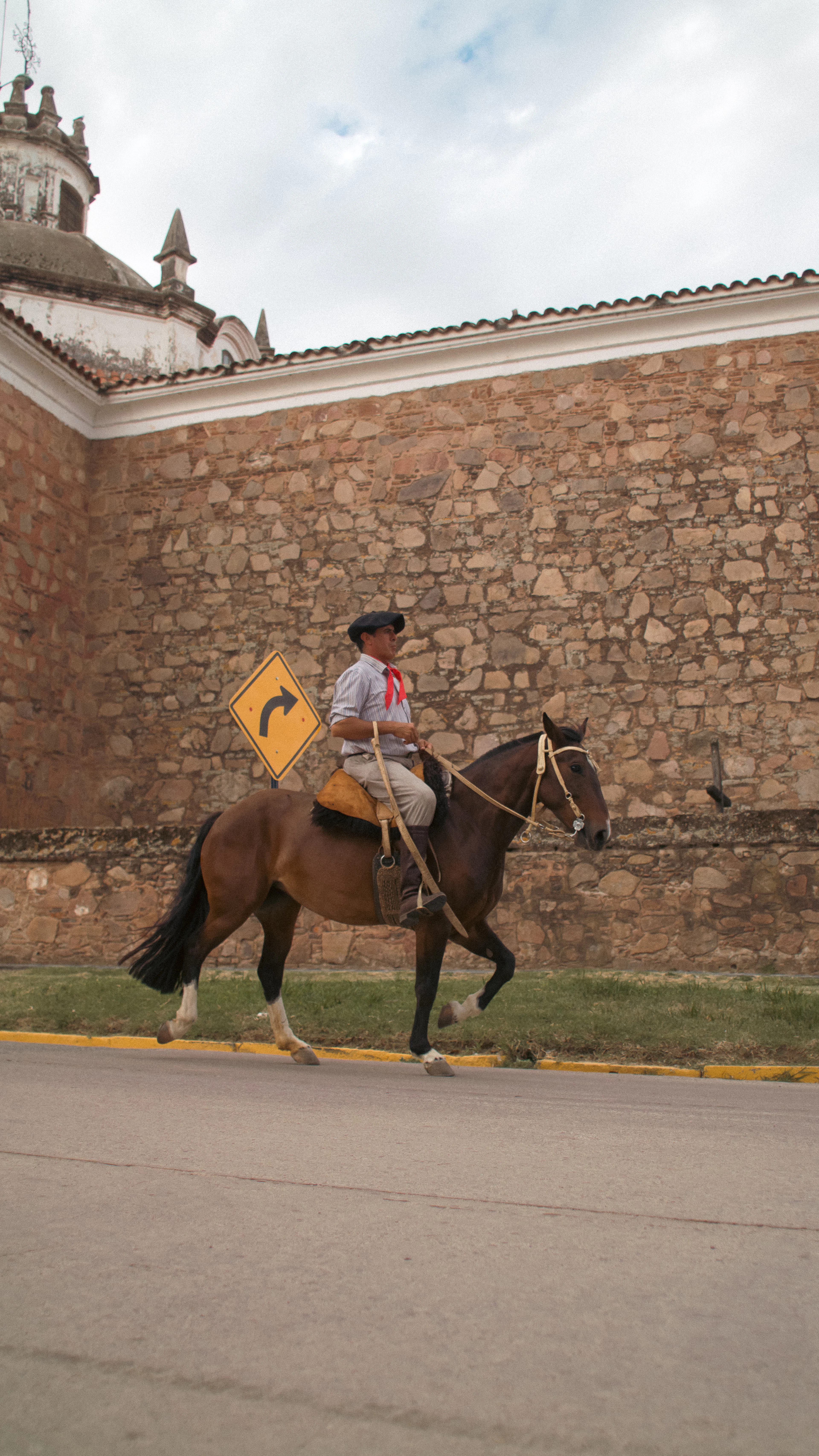 Jinete con boina y pañuelo rojo a caballo frente a un muro de piedra