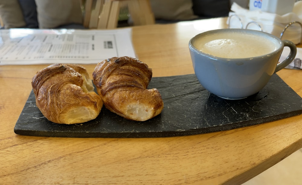 a couple of pastries on a black plate next to a cup of coffee