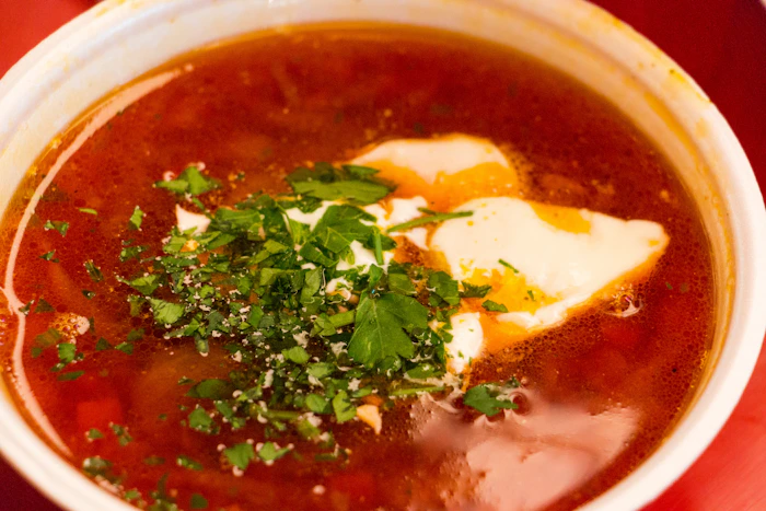 Bowl of red borscht soup topped with sour cream and chopped herbs