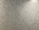 Geometric lines intersect across a textured grey surface, forming various angular shapes.