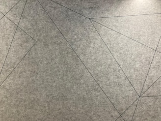 Geometric lines intersect across a textured grey surface, forming various angular shapes.