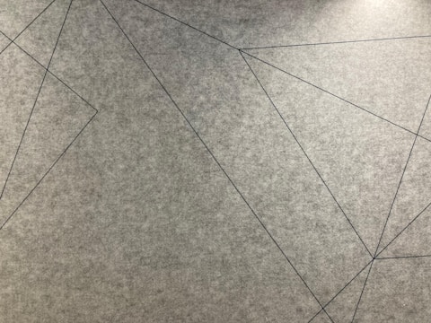 Geometric lines intersect across a textured grey surface, forming various angular shapes.