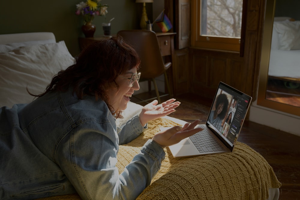 uma mulher sentada em uma cama usando um computador portátil