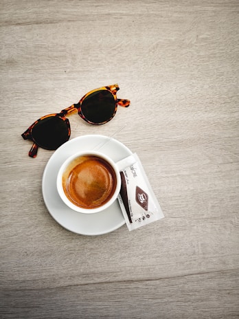 A stylish pair of sunglasses with sleek metal arms resting on an open travel journal beside a cup of coffee.