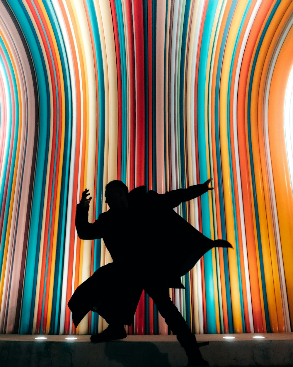 a silhouette of a person dancing in front of a multicolored wall