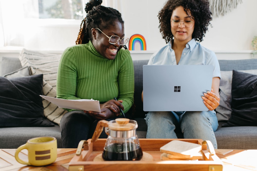 two women sitting on a couch looking at a laptop