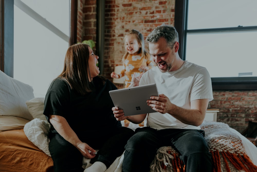 a man and a woman sitting on a bed looking at a tablet