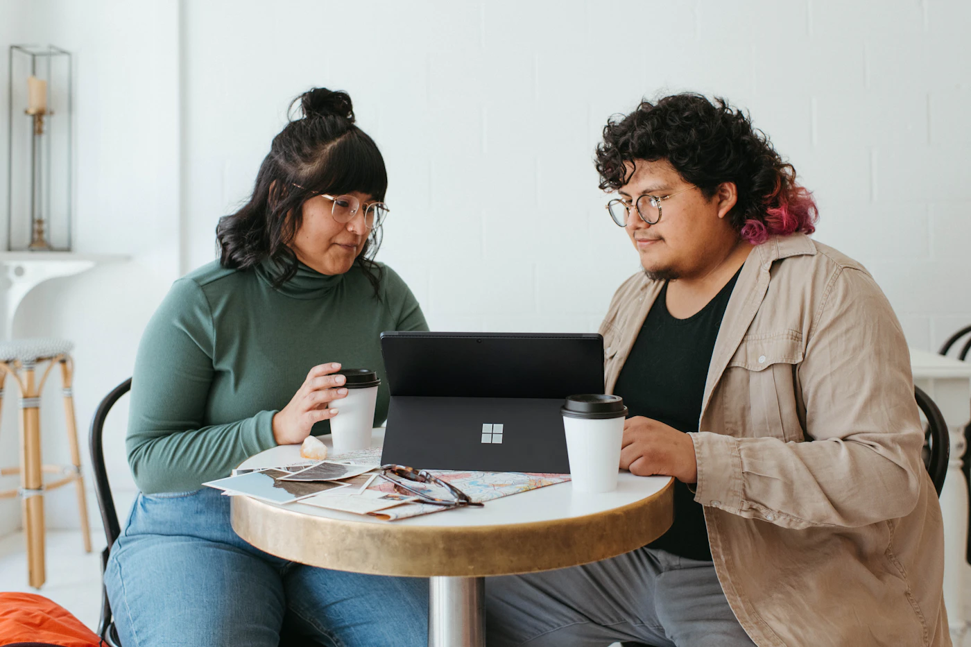 Two people at a small cafe table reviewing a laptop screen together over coffee
