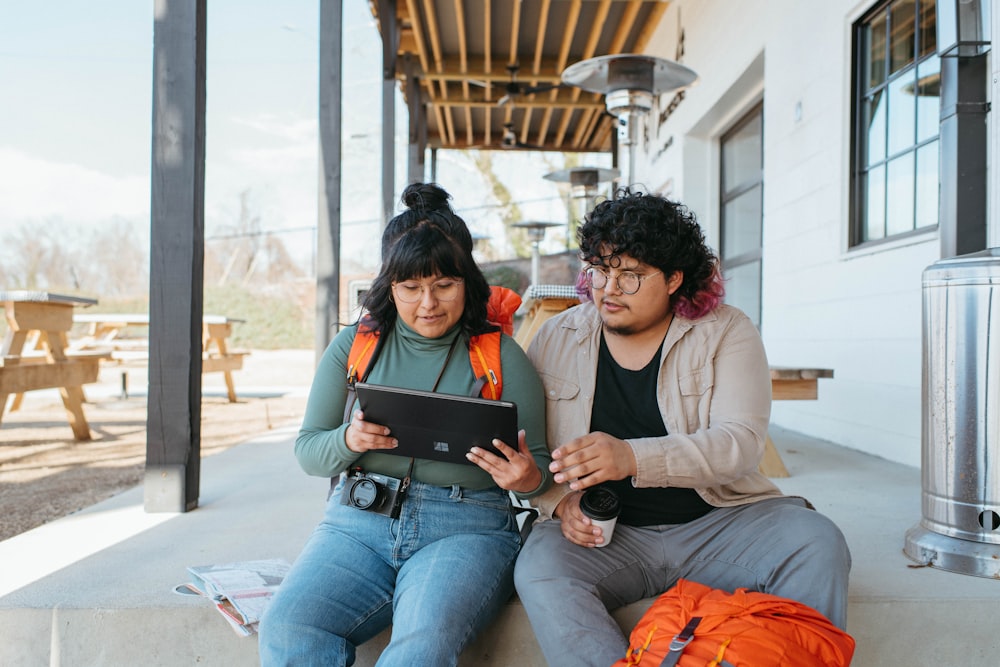 a man and a woman sitting on a porch looking at a tablet