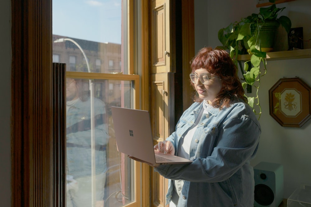 a woman standing in front of a window using a laptop computer