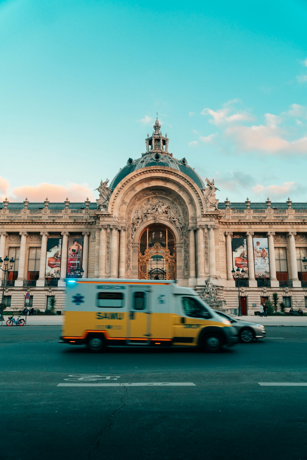 a yellow and white ambulance passing by a large building