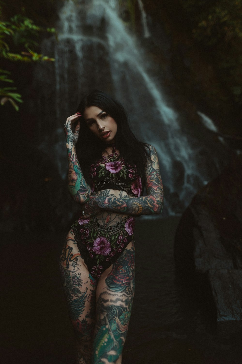 a woman with tattoos standing in front of a waterfall