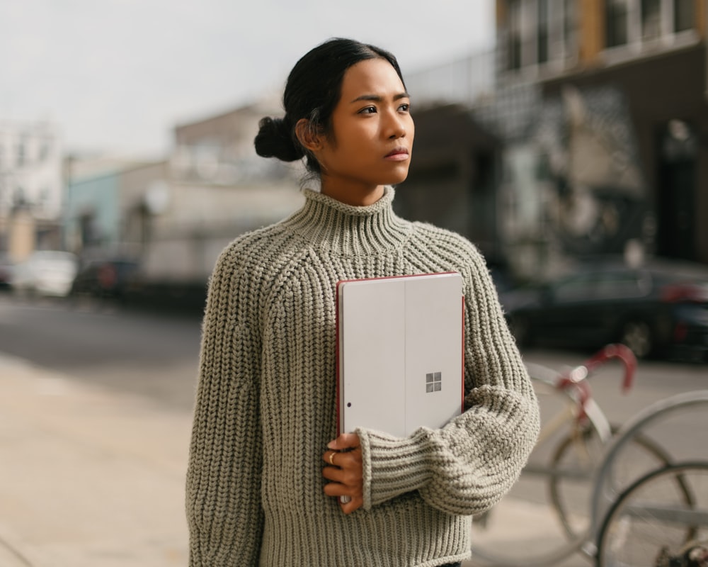 a woman standing on a sidewalk holding a laptop