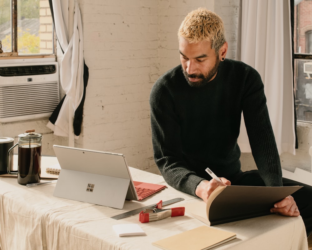 a man sitting at a table with a laptop and notebook