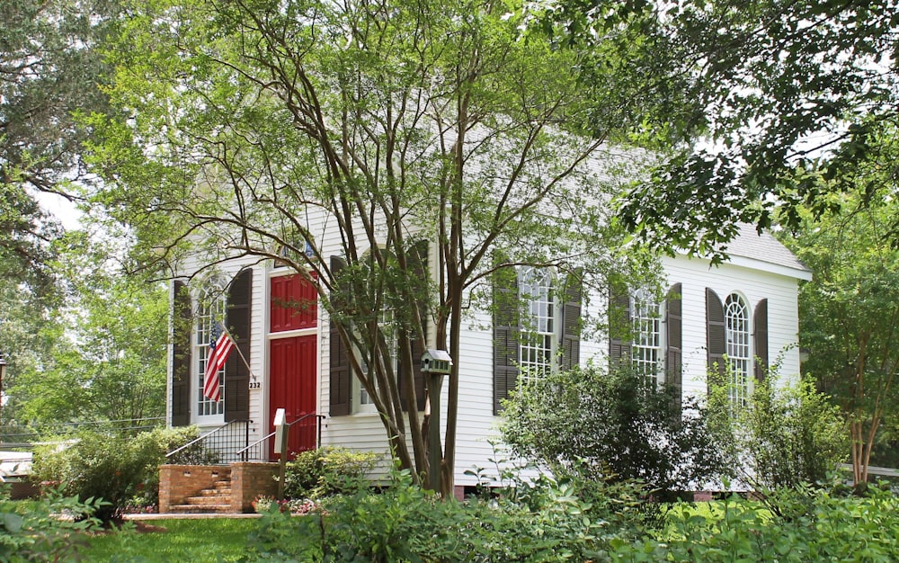a white house with a red door surrounded by trees