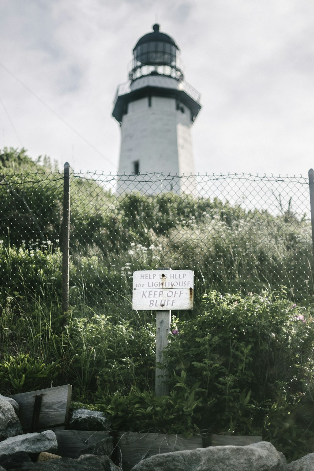 a sign in front of a fence with a light house in the background