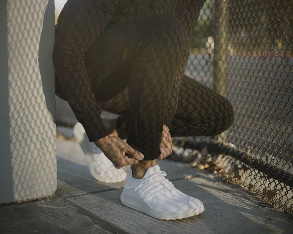 a man tying his white tennis shoes on the sidewalk