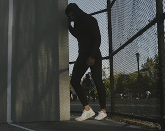 a man in a black hoodie leaning against a fence
