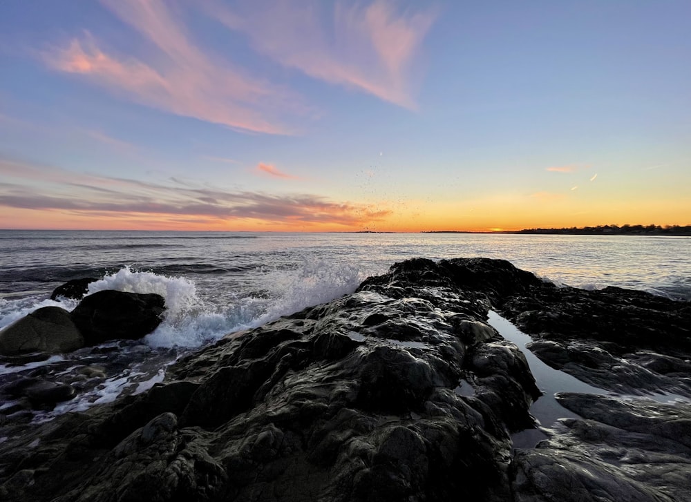 the sun is setting over the ocean with waves crashing on the rocks