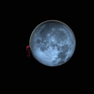 A large, detailed depiction of the moon with a prominent, cratered surface set against a dark backdrop. Adjacent to the moon is a small, red toy-like rocket ship, emphasizing a playful or imaginative theme.