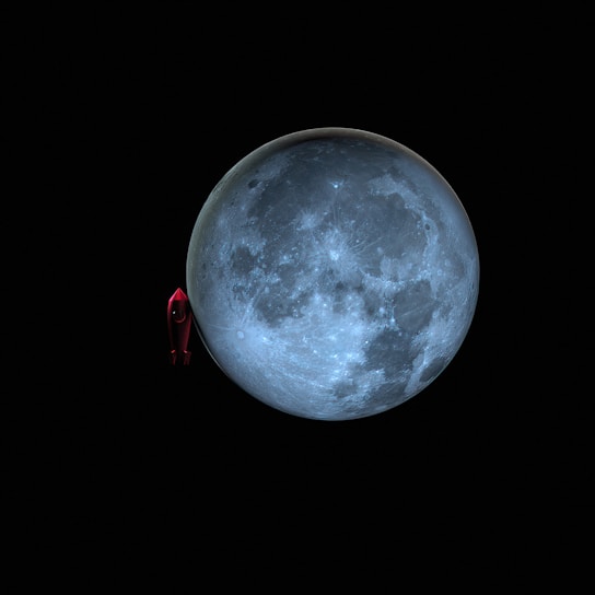 A large, detailed depiction of the moon with a prominent, cratered surface set against a dark backdrop. Adjacent to the moon is a small, red toy-like rocket ship, emphasizing a playful or imaginative theme.
