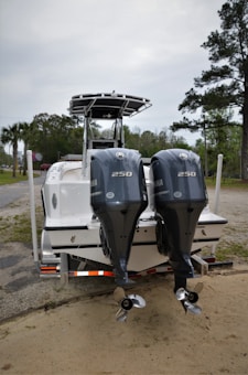 A boat is parked on a trailer with two powerful Yamaha outboard engines at the rear. The setting appears to be an outdoor area with trees and a cloudy sky in the background.