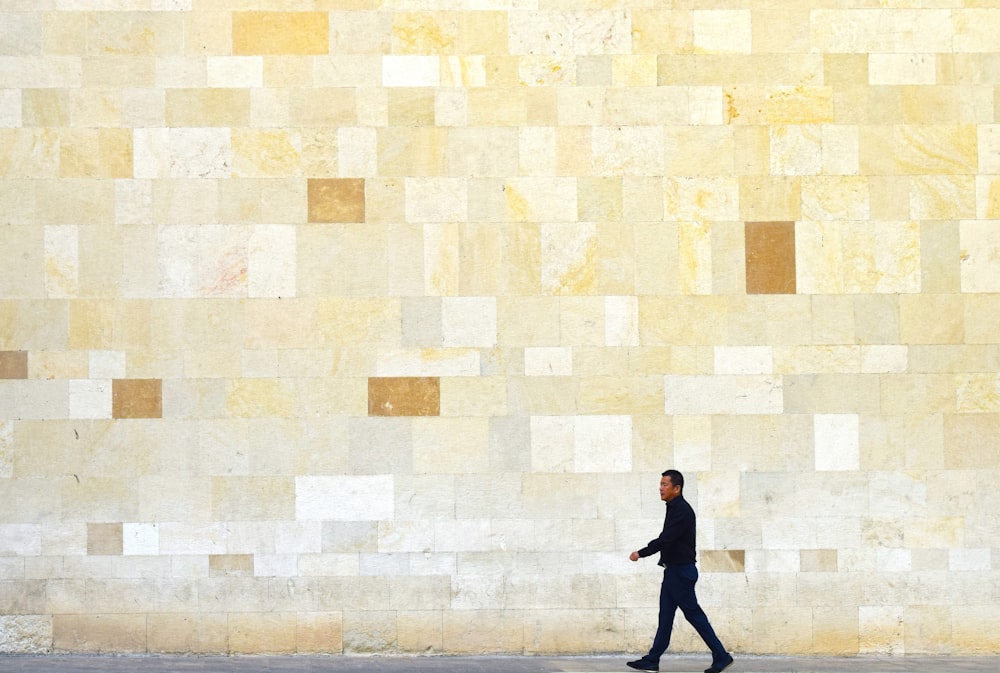 a man walking down a street past a wall