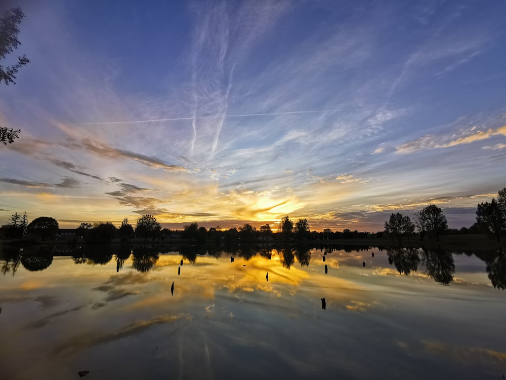 the sun is setting over a lake with trees in the foreground