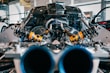 A close-up view of an intricate car engine, focusing on the suspension and shock absorber parts. The image captures the metallic and mechanical components, highlighting the yellow and black shock assemblies against a backdrop of carbon fiber and other engine elements.