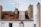 A rooftop characterized by red clay tiles and several chimneys. There are two skylights and an old-style television antenna perched on the roof. The wall beneath the roof is white, and the sky above is partly cloudy.