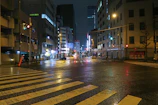 Close-up of dew-covered asphalt reflecting colorful traffic lights on an empty street corner at night.