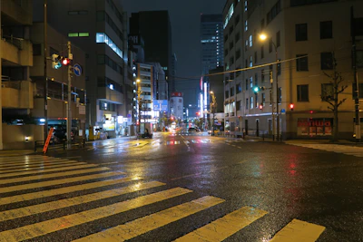 Close-up of dew-covered asphalt reflecting colorful traffic lights on an empty street corner at night.