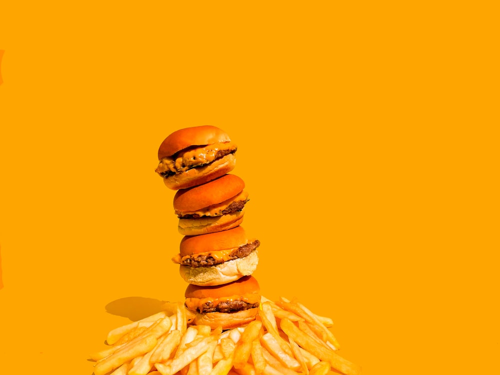a stack of hamburgers and french fries on a yellow background