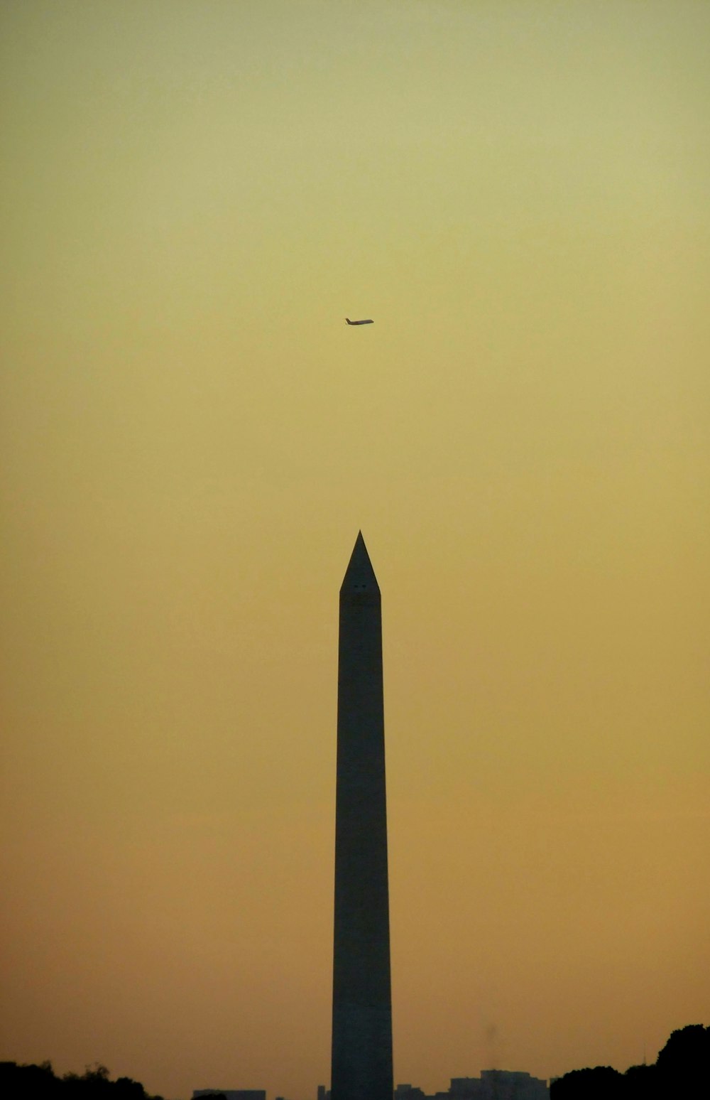 a plane flying over the washington monument at sunset