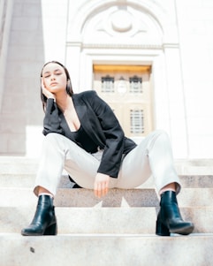 A man standing confidently on marble steps wearing luxurious black and gold boots, with a deep maroon cloak flowing behind him.