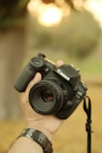 A photographer adjusting a DSLR camera lens outdoors during golden hour.