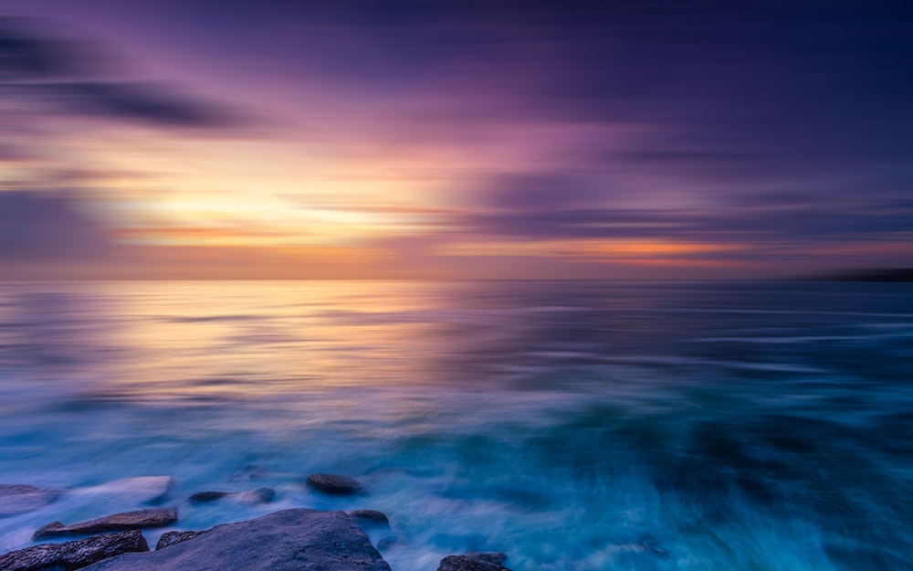 a sunset over the ocean with rocks in the foreground