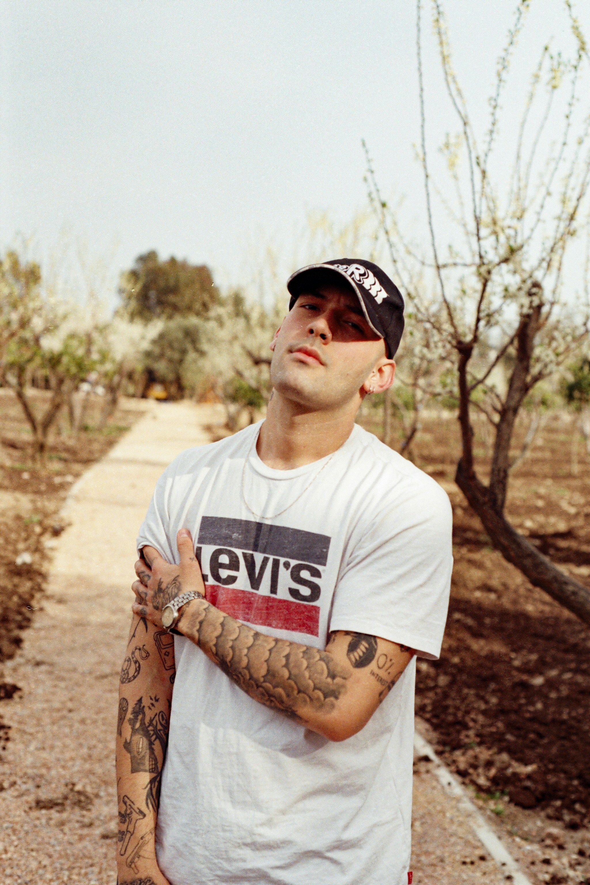a man with tattoos standing on a dirt road