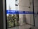 Glass doors with blue signage displaying 'World University of Bangladesh.' The background features a railing and some trees, indicating an outdoor view. The space appears to be part of a modern building design.
