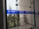 Glass doors with blue signage displaying 'World University of Bangladesh.' The background features a railing and some trees, indicating an outdoor view. The space appears to be part of a modern building design.