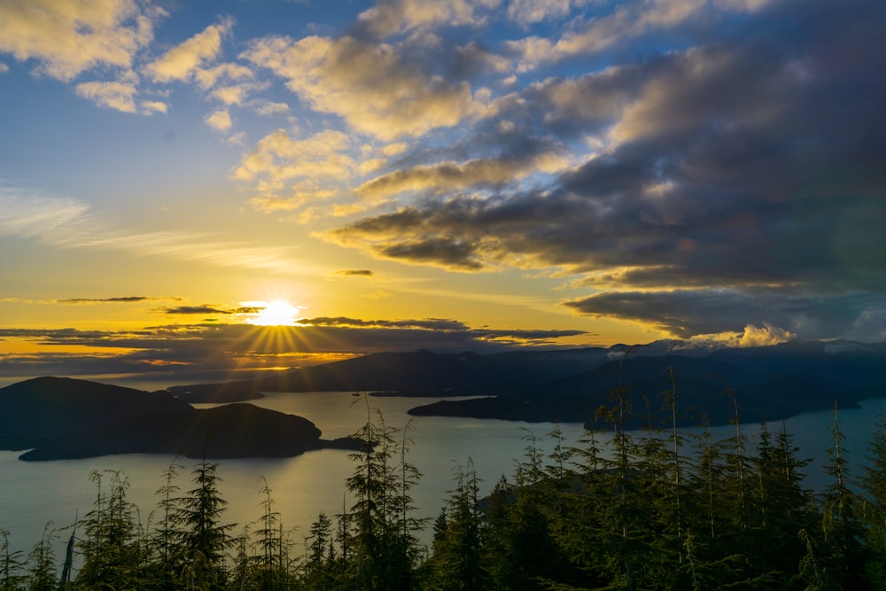 the sun is setting over a lake surrounded by mountains